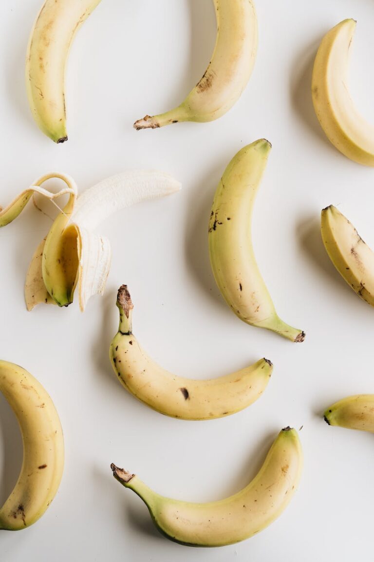 Ripe bananas arranged on a white surface, one peeled