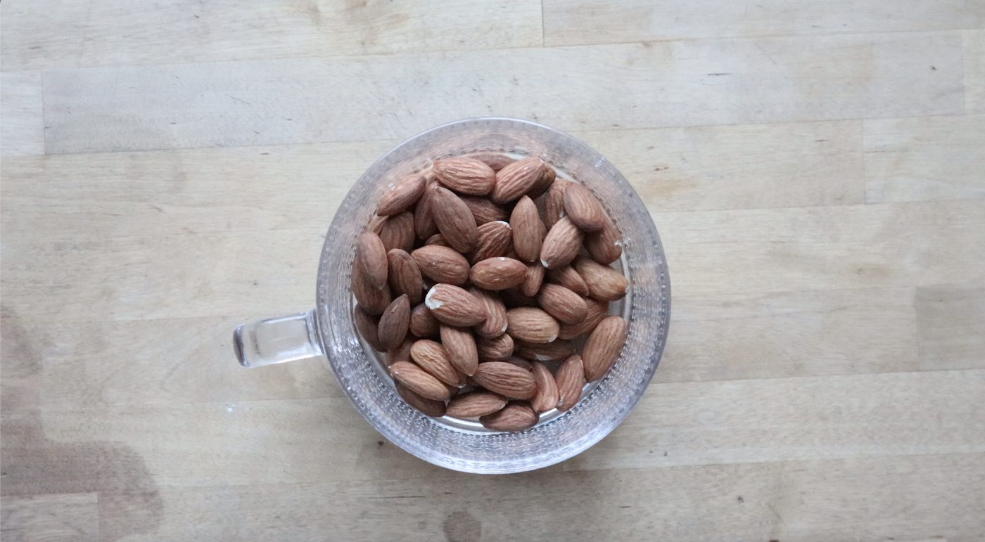 Whole almonds added to a glass mug as the first step of chia seed parfait