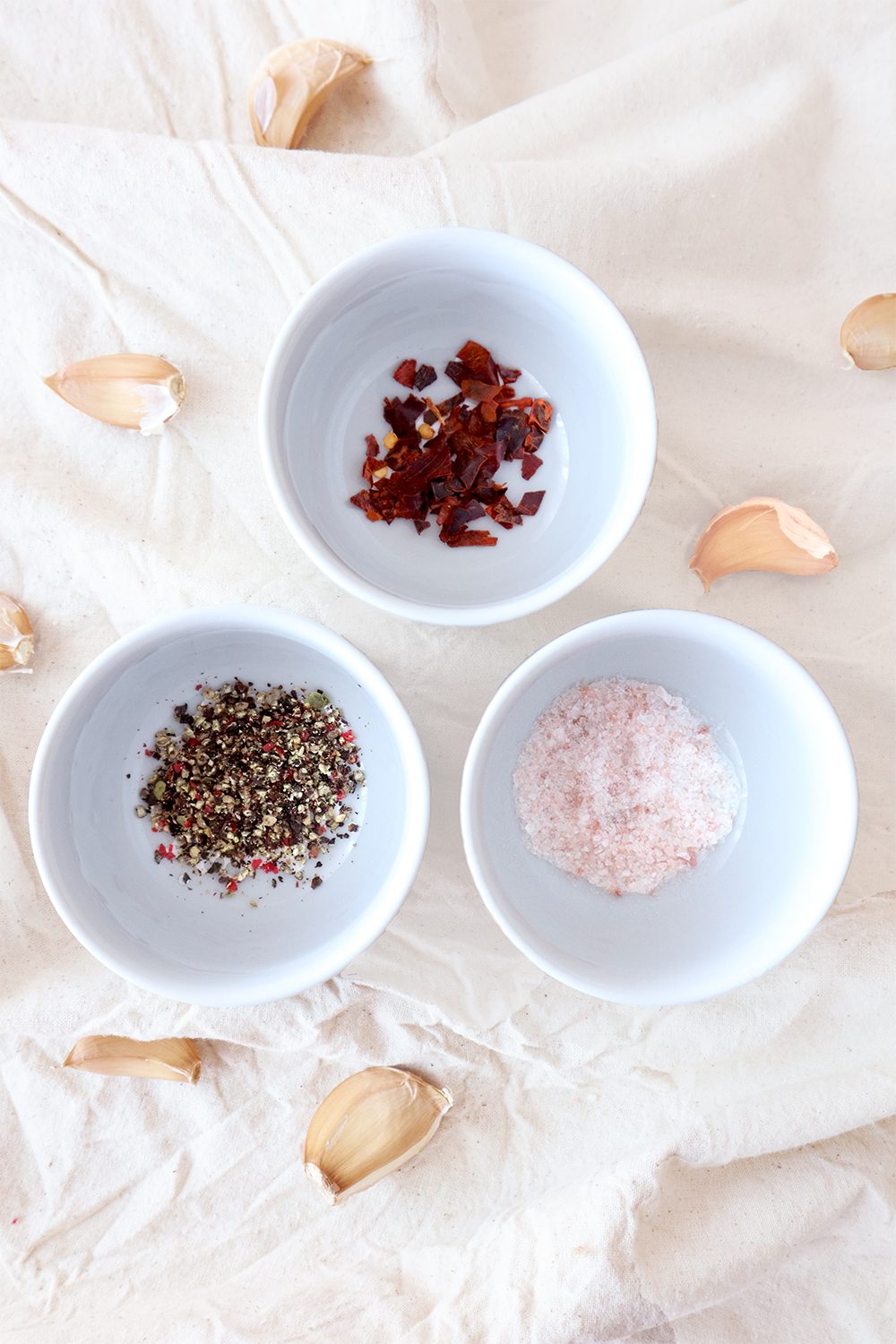 Bowls of salt, black pepper, and red chili flakes with garlic cloves